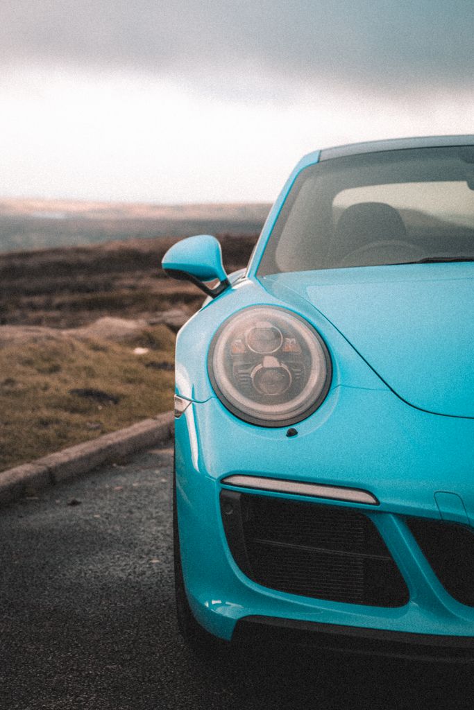 Dynamic shot capturing a blue sports car on an open road with Manchester's countryside backdrop.